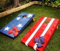 American Flag decorated corn hole boards on trim green lawn with landscaped border