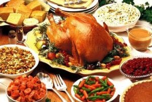 Thanksgiving feast of turkey surrounded stuffing, cornbread, mashed potatoes, gravy, cranberries, pie, vegetables, and yams