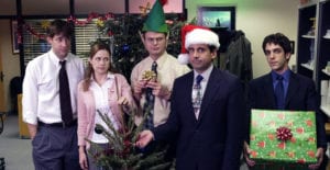 Cast of the American tv show "The Office" at Christmas party Jim, Pam, Dwight in elf hat, Michael Scott in Santa hat, and Ryan holding green present