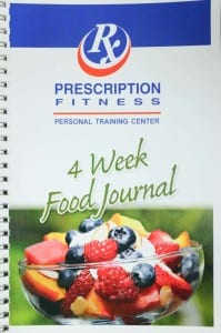 Spiral notebook of blue, white, and red 4 week food journal with bowl of fruit salad