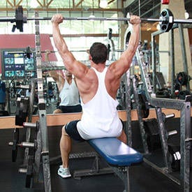 Muscular man lifting barbell on blue bench in gym
