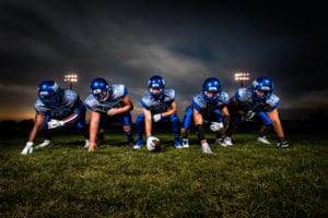 Five football players in blue uniforms playing football under the lights
