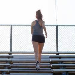 Young woman in gray and black running up empty bleacher steps