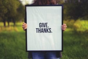 Person holding black framed give thanks sign outside in early fall