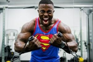 Muscular smiling african american in blue superman shirt lifting weights in gym