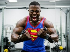 Muscular smiling african american in blue superman shirt lifting weights in gym