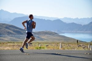Man wearing blue and black running on road with mountains and lake in background