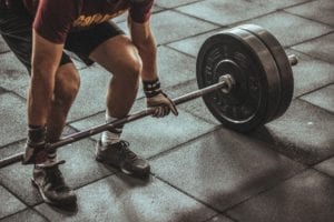 Man in red shirt and black shorts lifting weights off tile floor