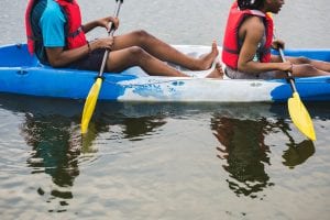 Two people wear life jackets paddling on blue kayak