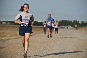 Woman in blue running ahead of group of other runners outside on a dirt road