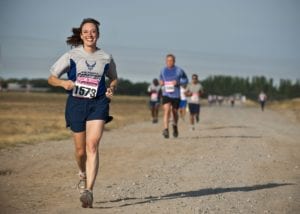 Woman in blue running ahead of group of other runners outside on a dirt road