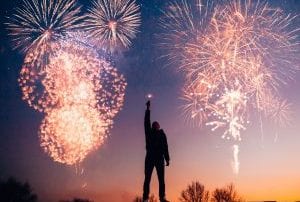 Man holding sparkler at sundown with fireworks going off