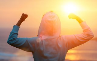 Back view of strong motivated woman celebrating workout goals towards the sun.