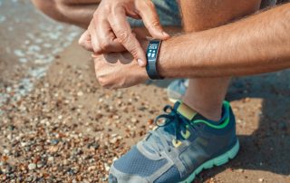 Male athlete checking step count in smart wristband at the seashore in summer