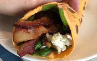 Hand holding sweet potato wrap on plate filled with food.